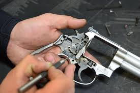 A person's hands are shown working on the intricate internal mechanism of a disassembled silver revolver, using a small tool.